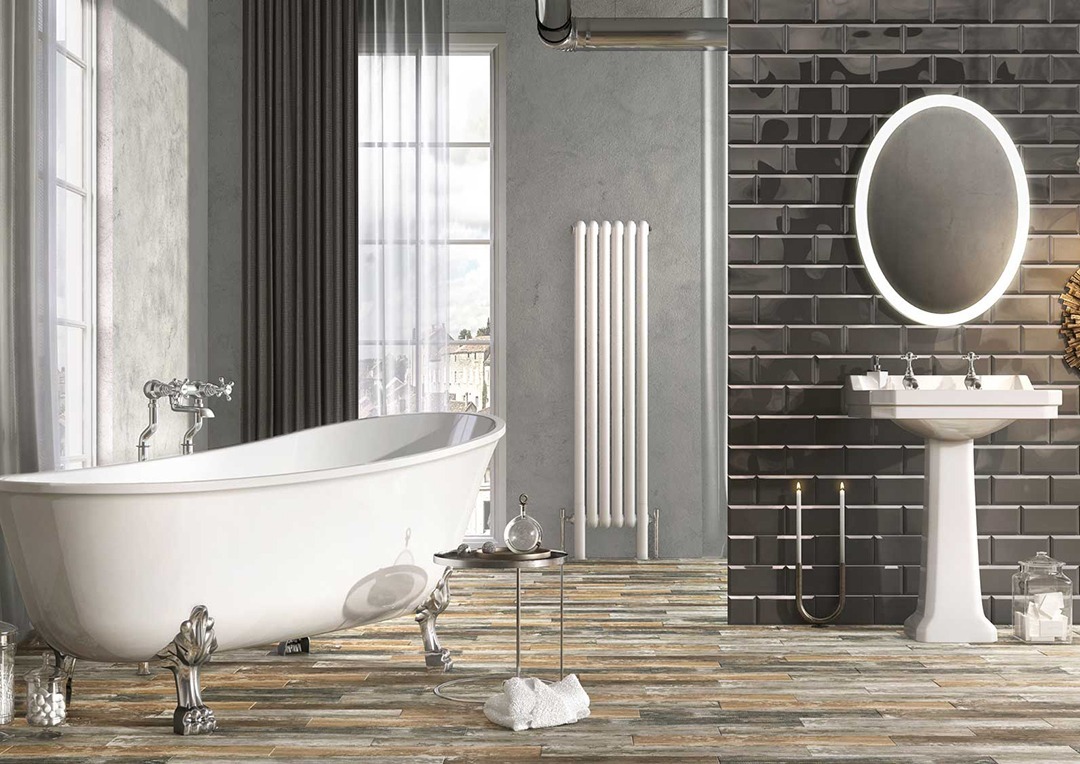 Deep claw foot bath, white with silver feet. Wooden Floor and exposed brick wall.